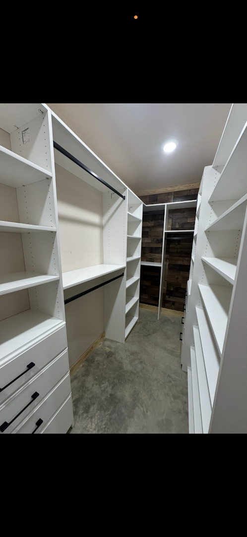 Custom walk-in closet with white shelving, drawers, and a wood accent wall